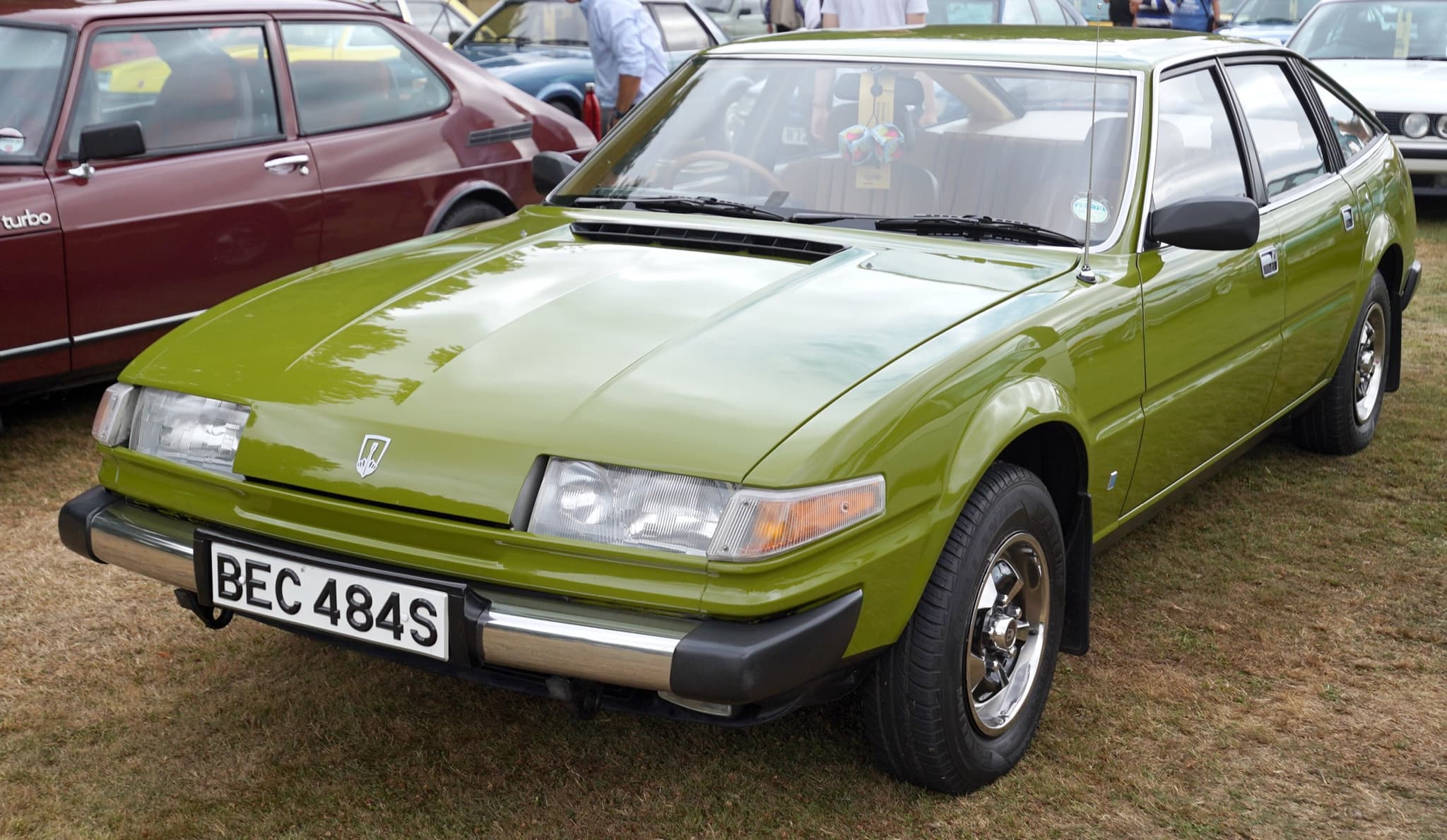 A green Rover 3500 hatchback with chrome bumpers on a showground, other cars behind it.