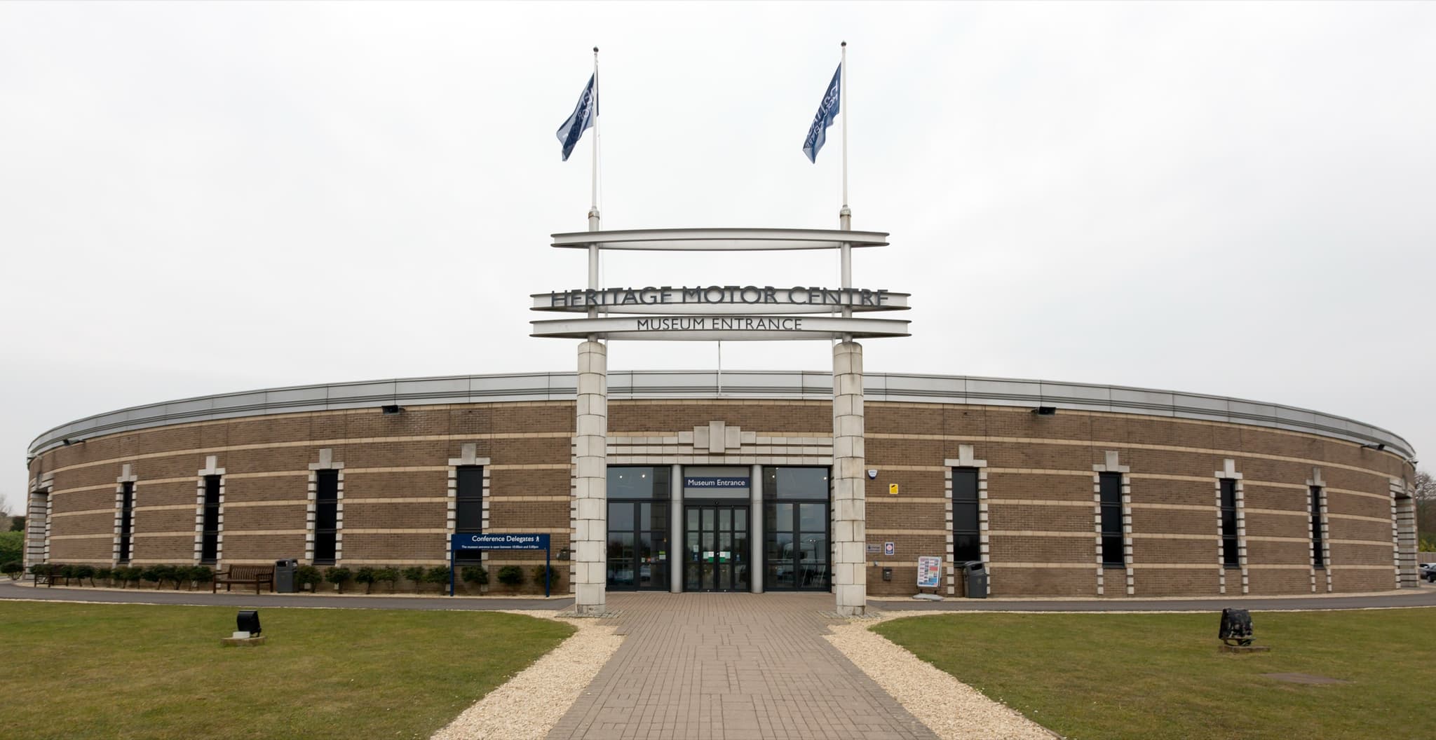 The circular brick museum building at Gaydon behind a lawn, its entrance sign reading Heritage Motor Centre.