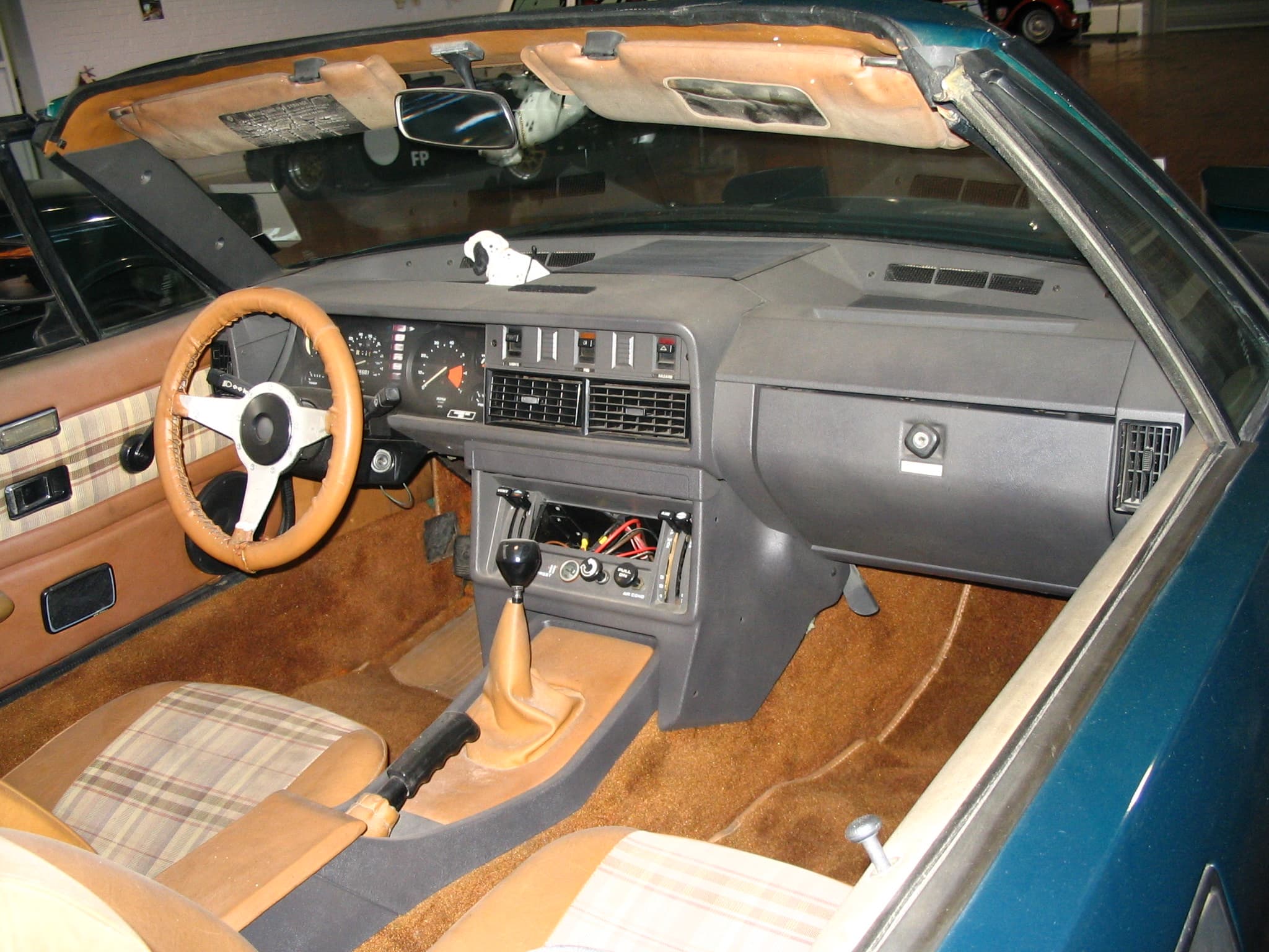 The cockpit of a TR8 convertible: plaid seat inserts, a small leather-rimmed three-spoke wheel and a grey dashboard.