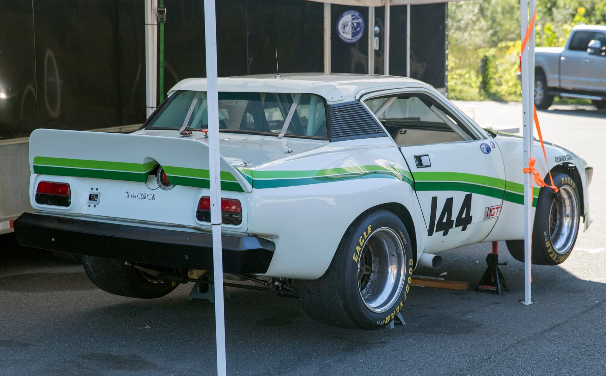 The white and green racing TR8 from the rear, with a tall rear wing, wide slicks and a roll cage.
