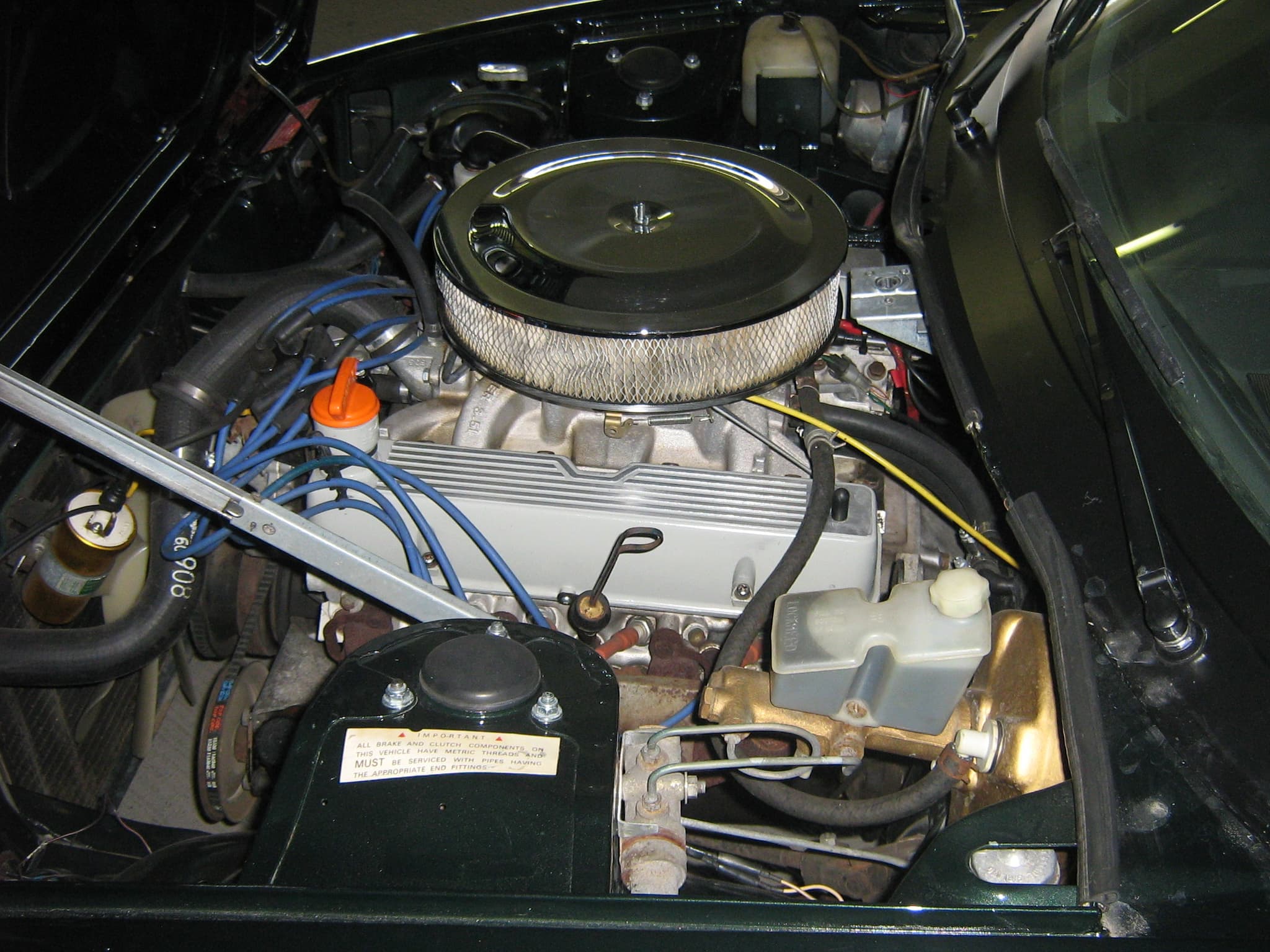 A TR8's V8 lit by flash, with a chrome round air cleaner on an aftermarket four-barrel carburettor.